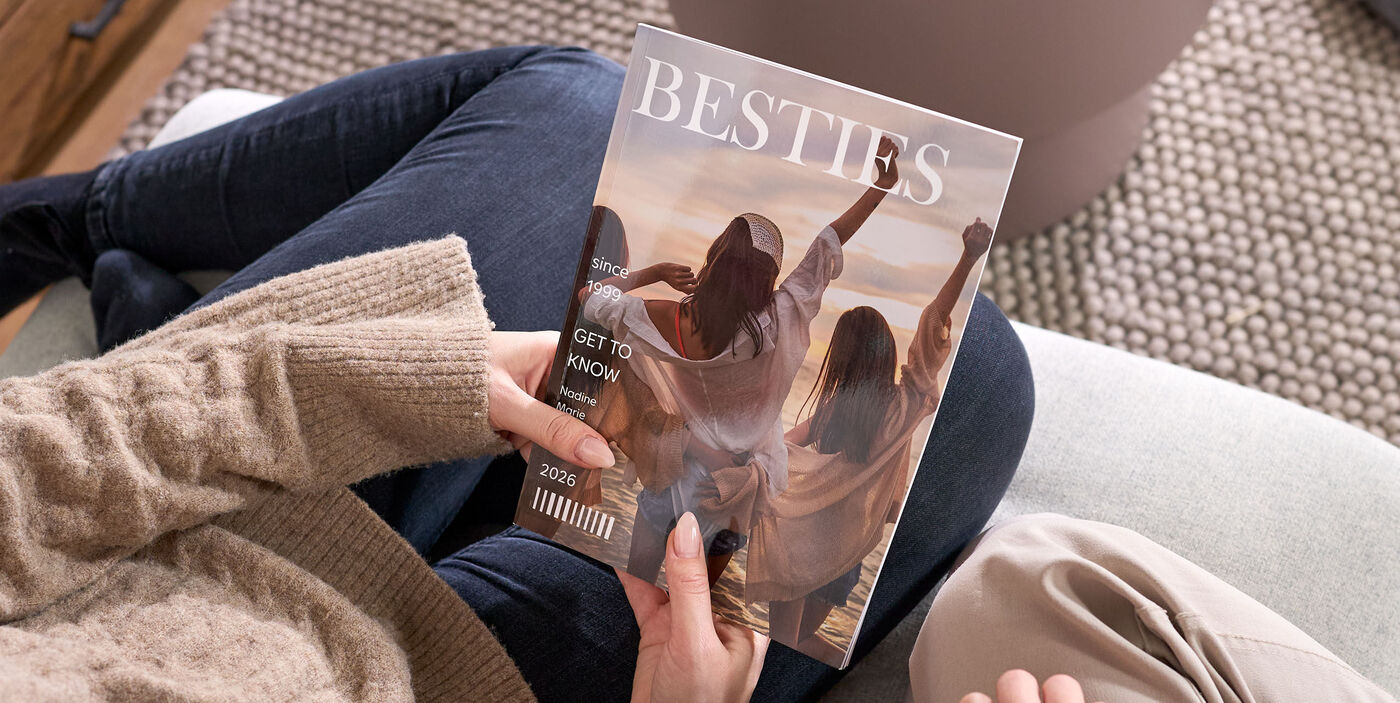 Két ember ül egy kanapén, és egy becsukott magazint néz, amelynek címlapján három, háttal álló nő látható a tengerparton, és a „BESTIES” felirat olvasható.